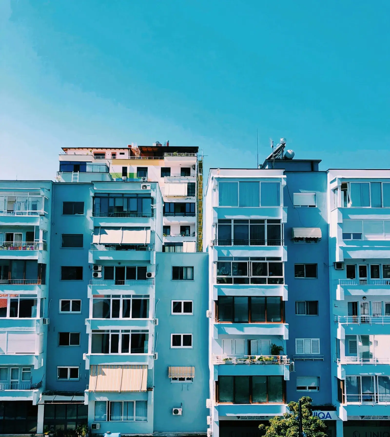 Fasada blu e pallateve të banimit në Tiranë, me ballkone, tenda dhe panele diellore në tarracë