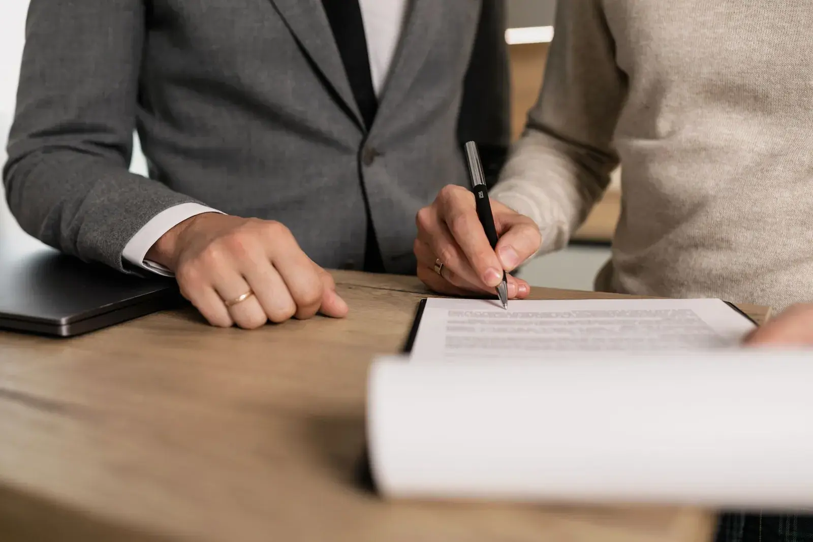 A hand signing a contract on a wooden table