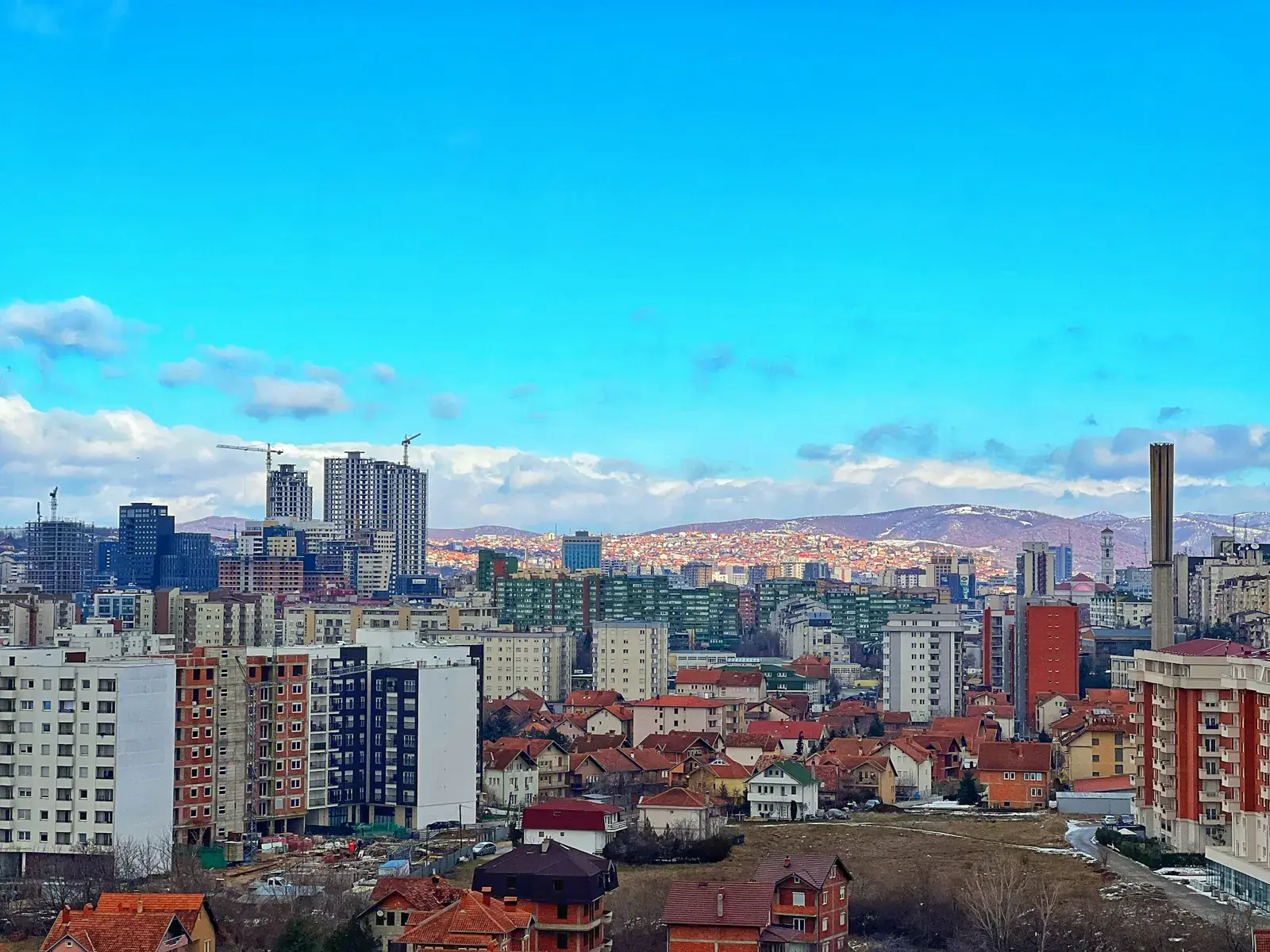 Pallate banimi dhe kulla të reja në Prishtinë, me shtëpi me çati të kuqe dhe kodra në sfond