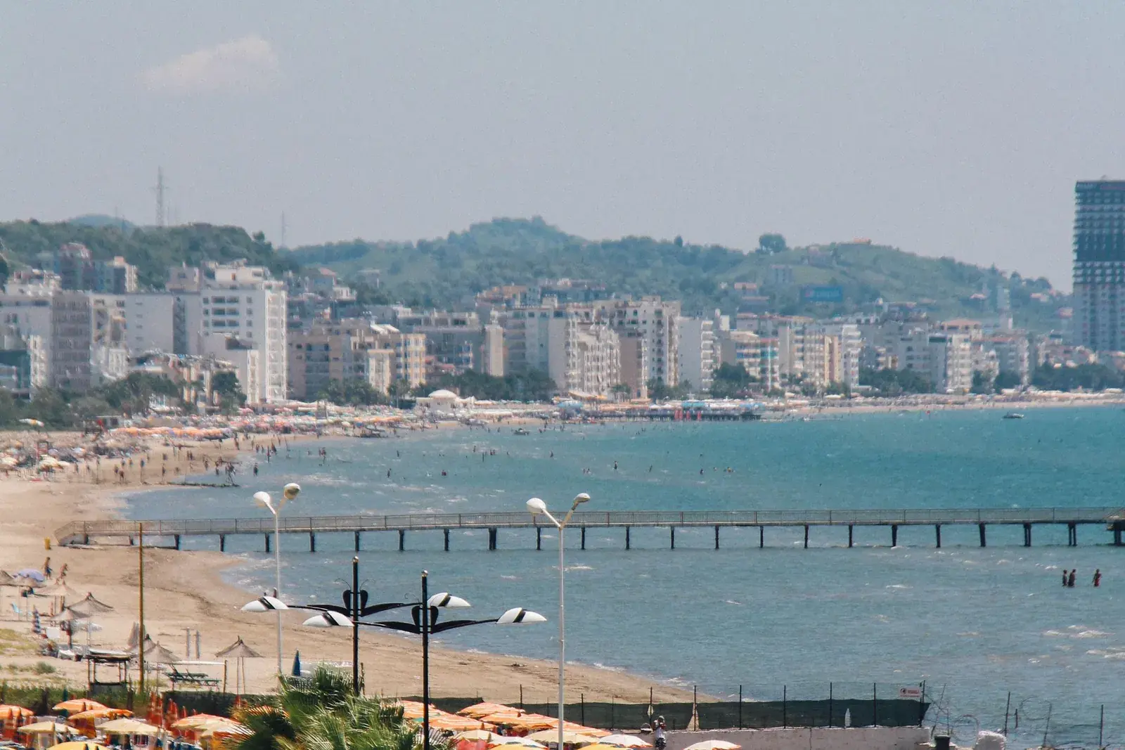 La spiaggia di Durazzo d'estate con palazzi sul lungomare, un pontile e ombrelloni