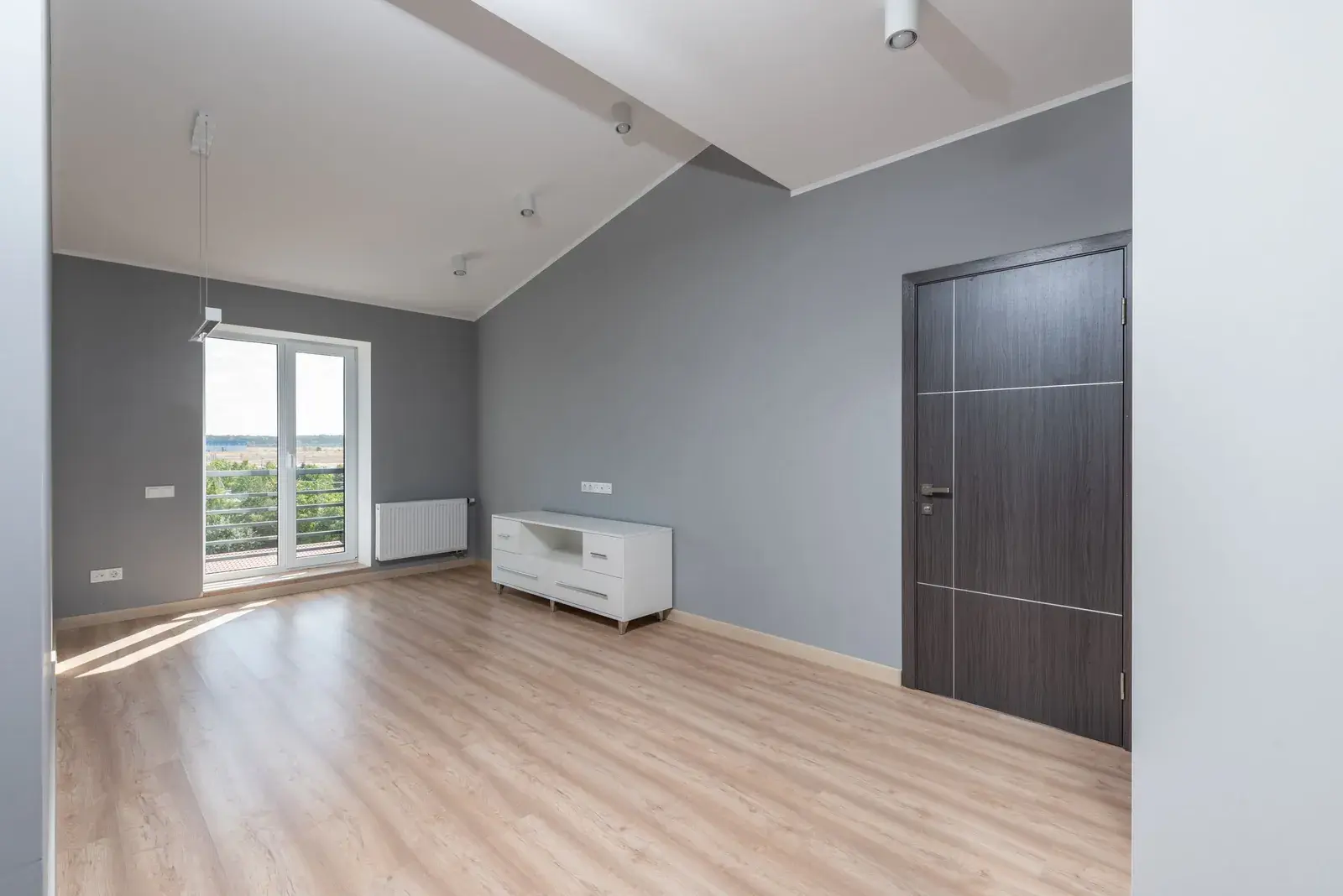 Bright, empty apartment room with a wooden floor and a balcony door