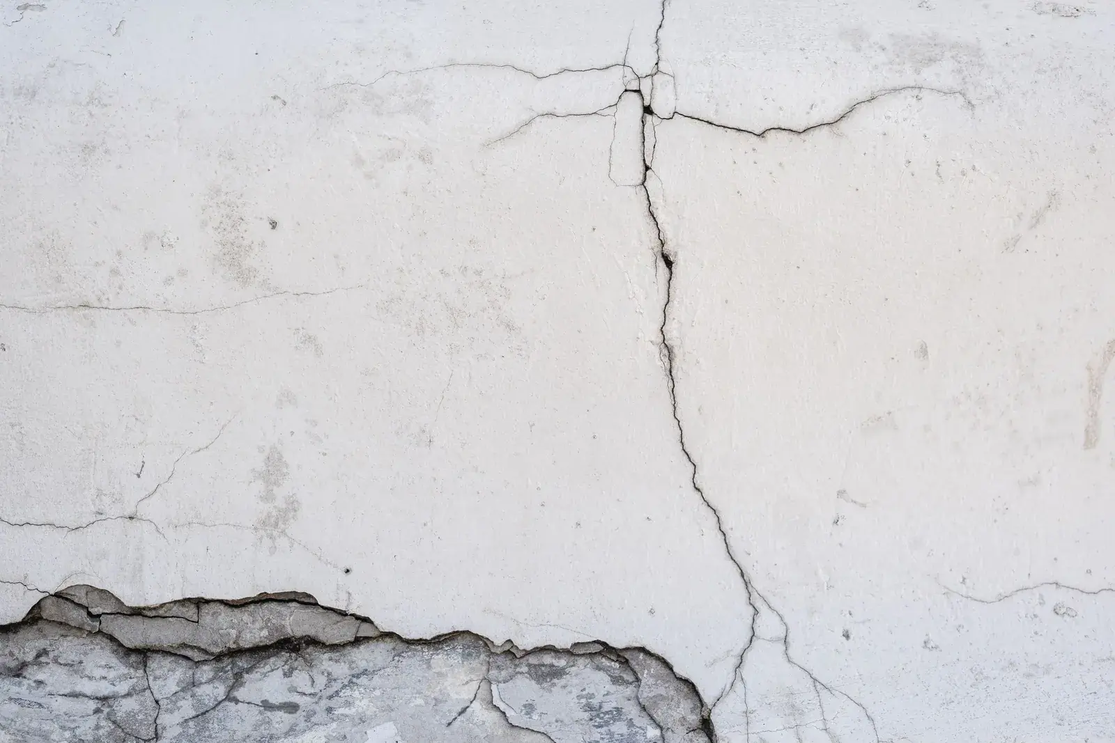 Una lunga crepa nell'intonaco di un muro bianco, con l'intonaco staccato in basso