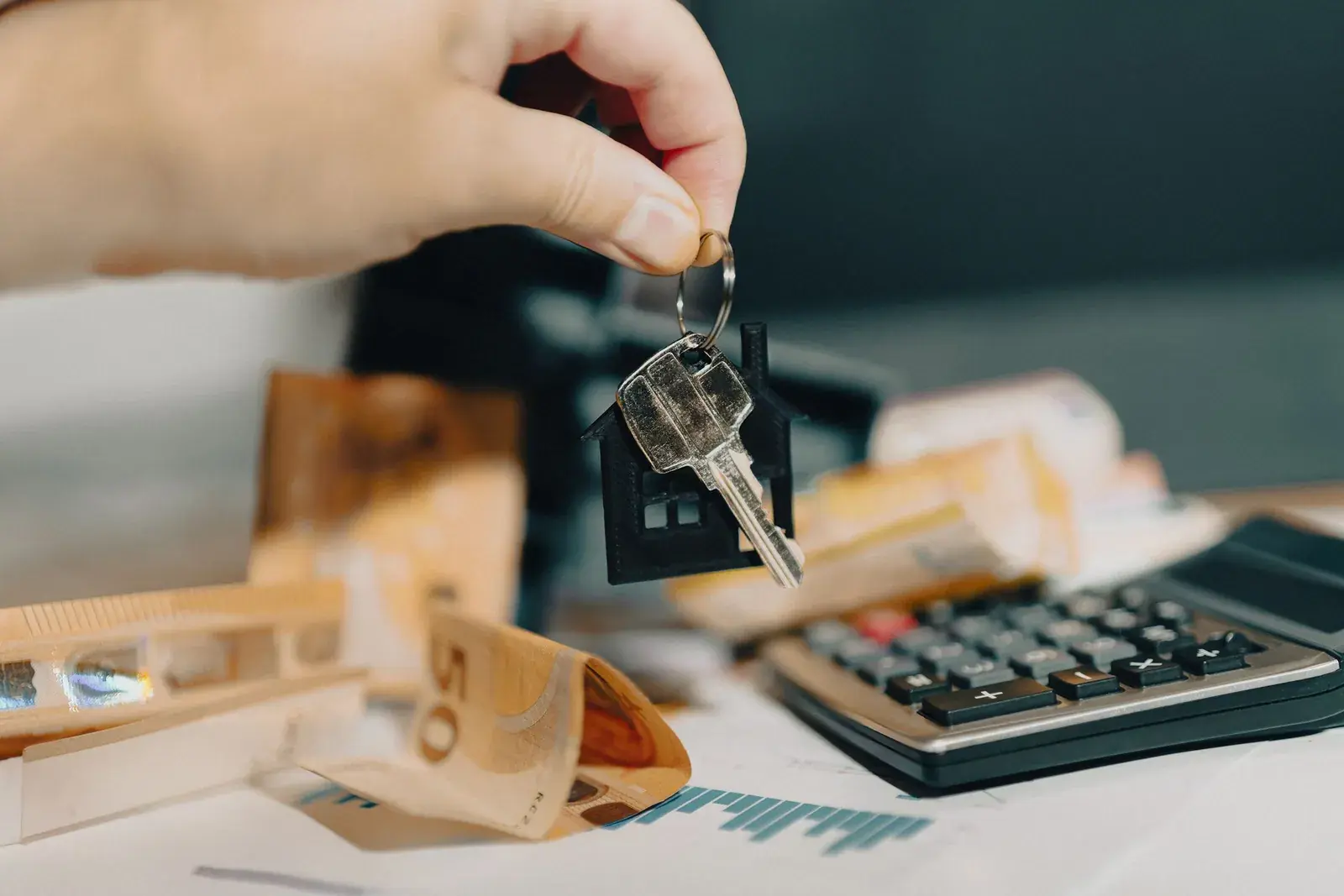 Hand holding house keys above euro banknotes and a calculator