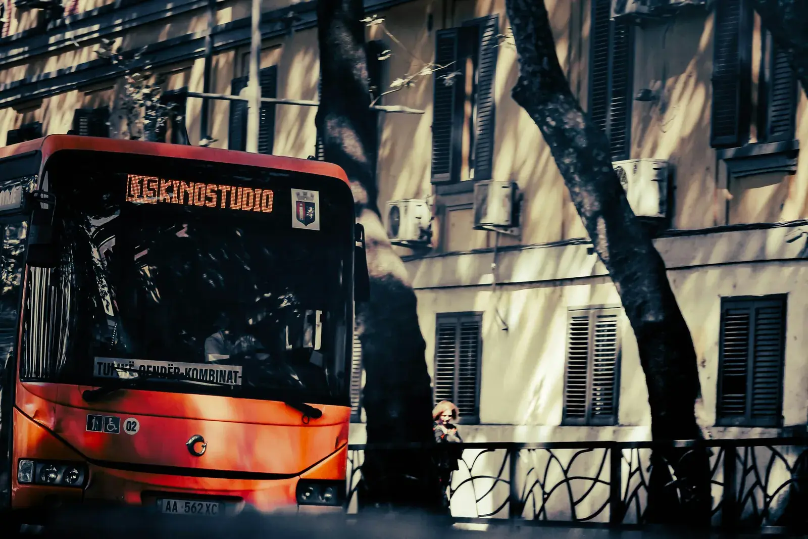 Autobus i kuq i linjës urbane para një pallati me grila në Tiranë