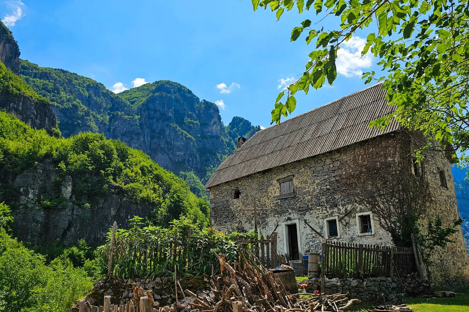 Old stone house with a wooden roof in Theth, surrounded by green mountains