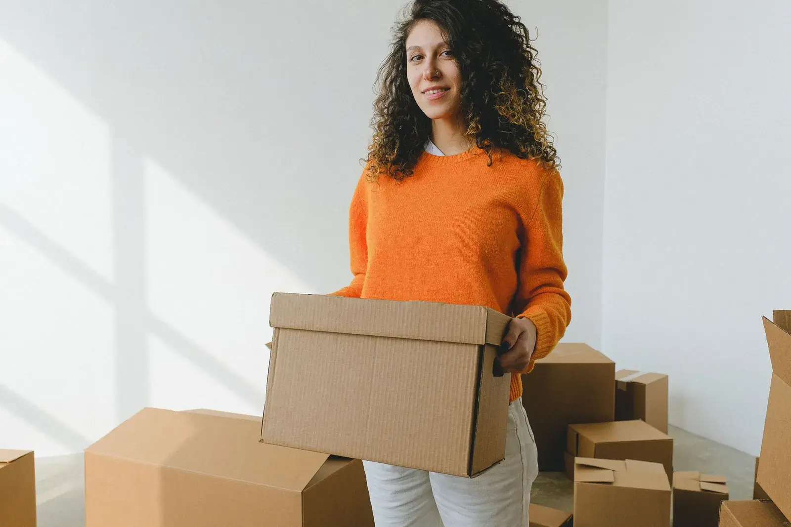Young woman holding a cardboard box on moving day in her new rented flat