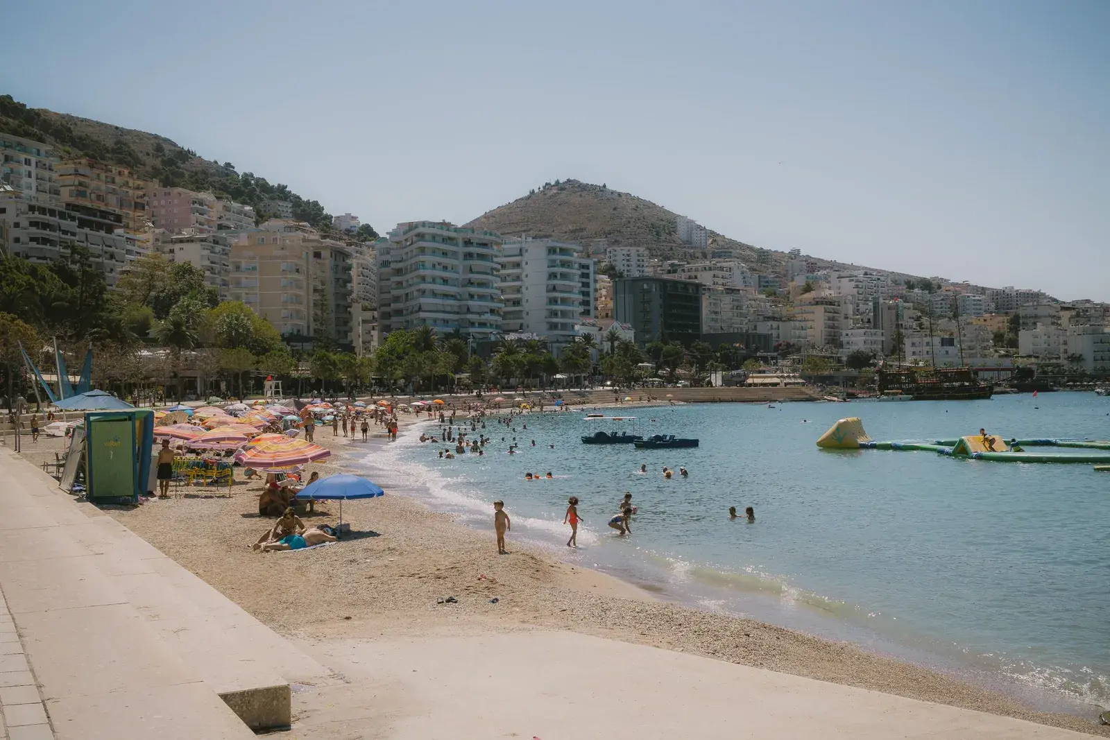 Plazhi i qytetit në Sarandë me pallatet e vijës së parë pas shëtitores në një ditë vere