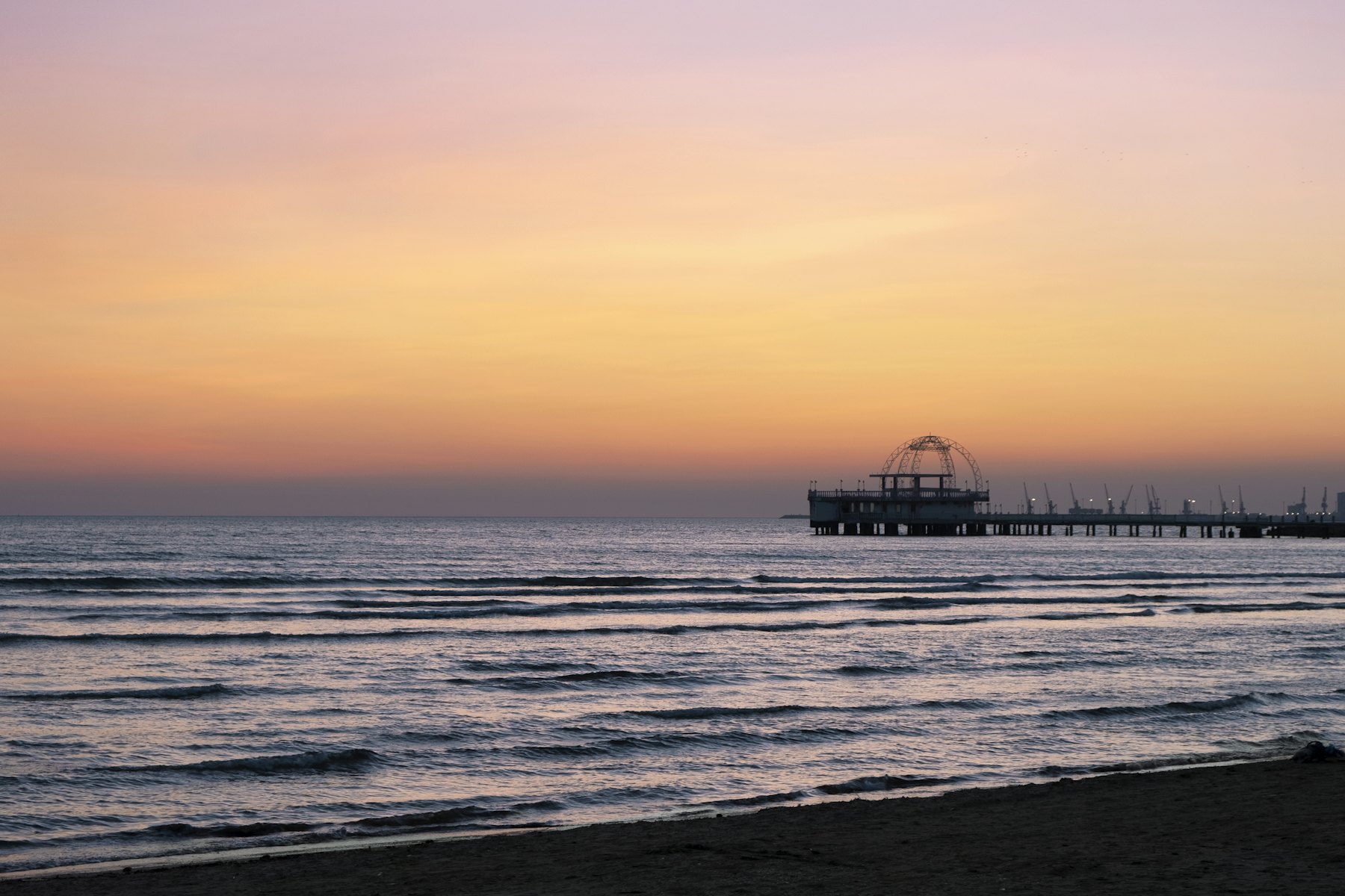 a sunset view of a beach with a pier in the distance