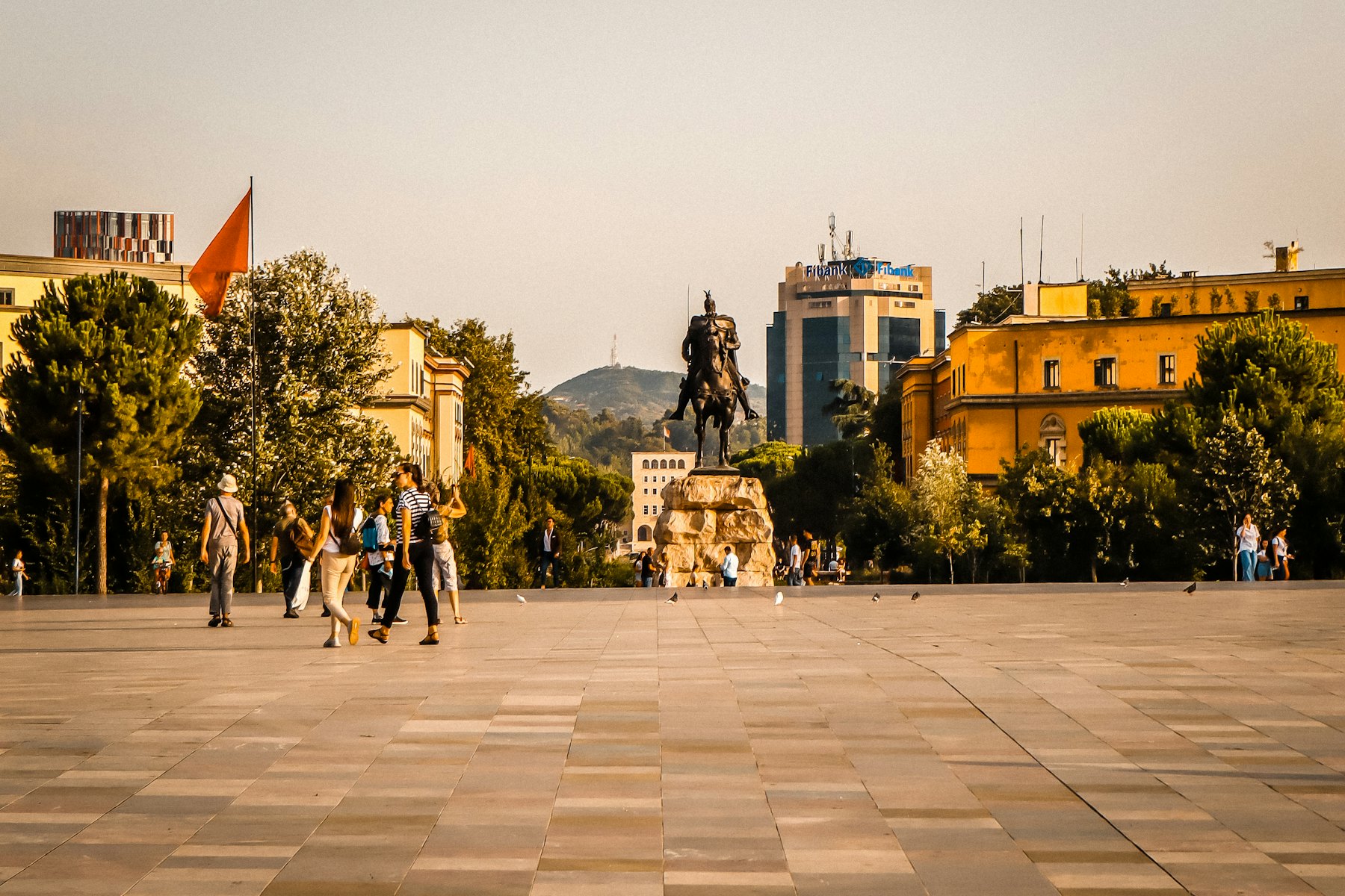 People walk in a city square with a statue