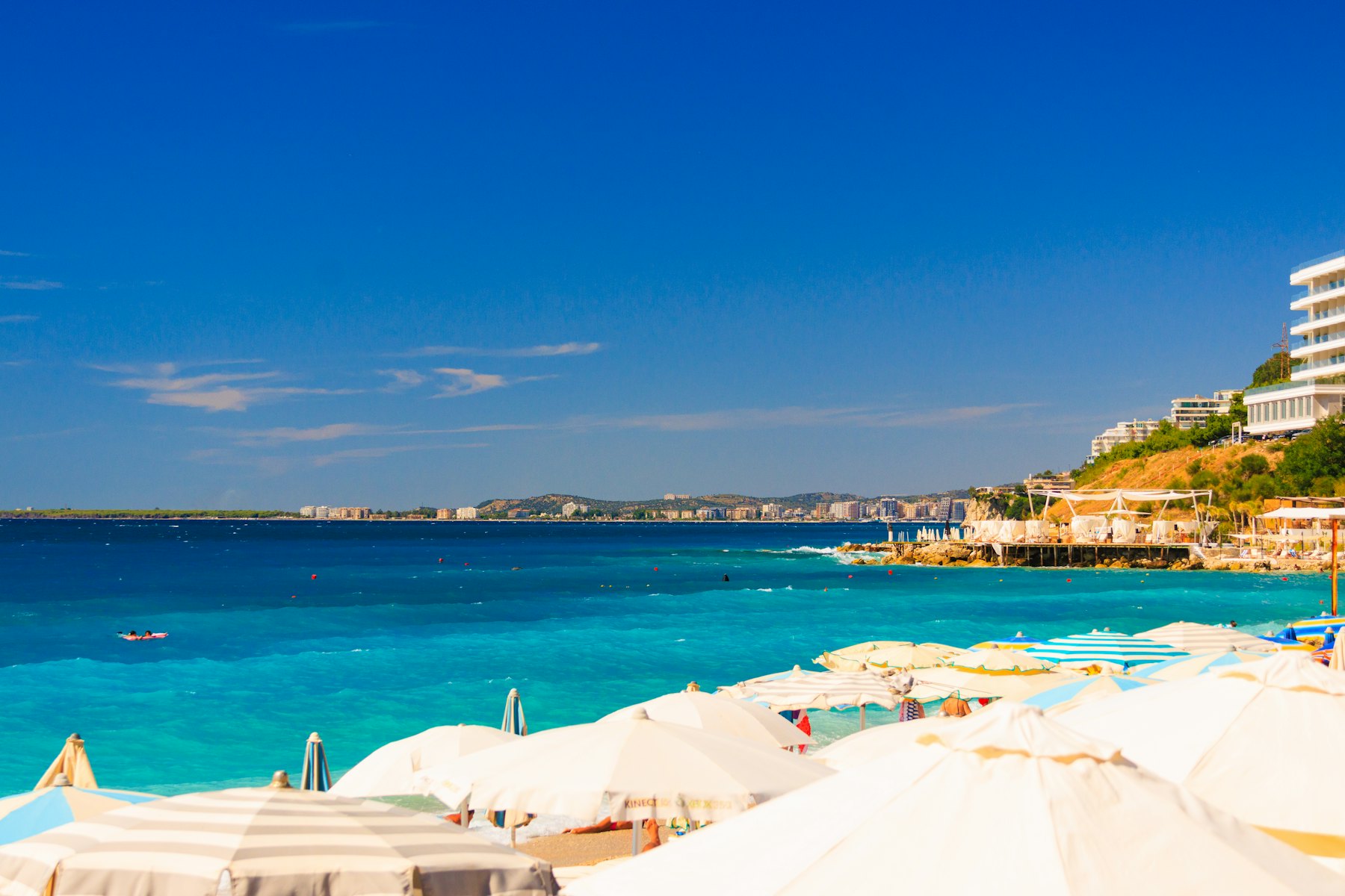 White beach umbrellas on a turquoise sea shore with a distant coastal city