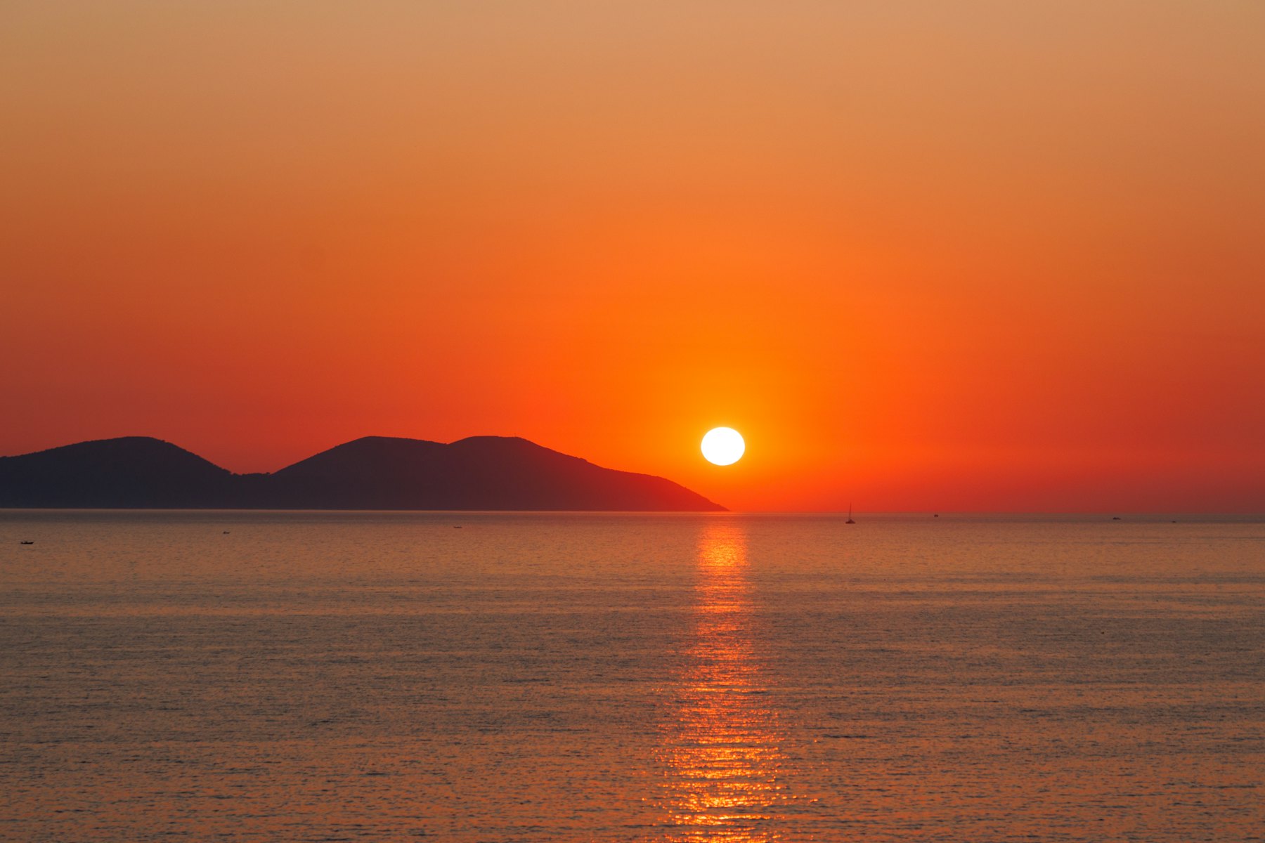 Low sun over a calm sea with a distant island silhouette
